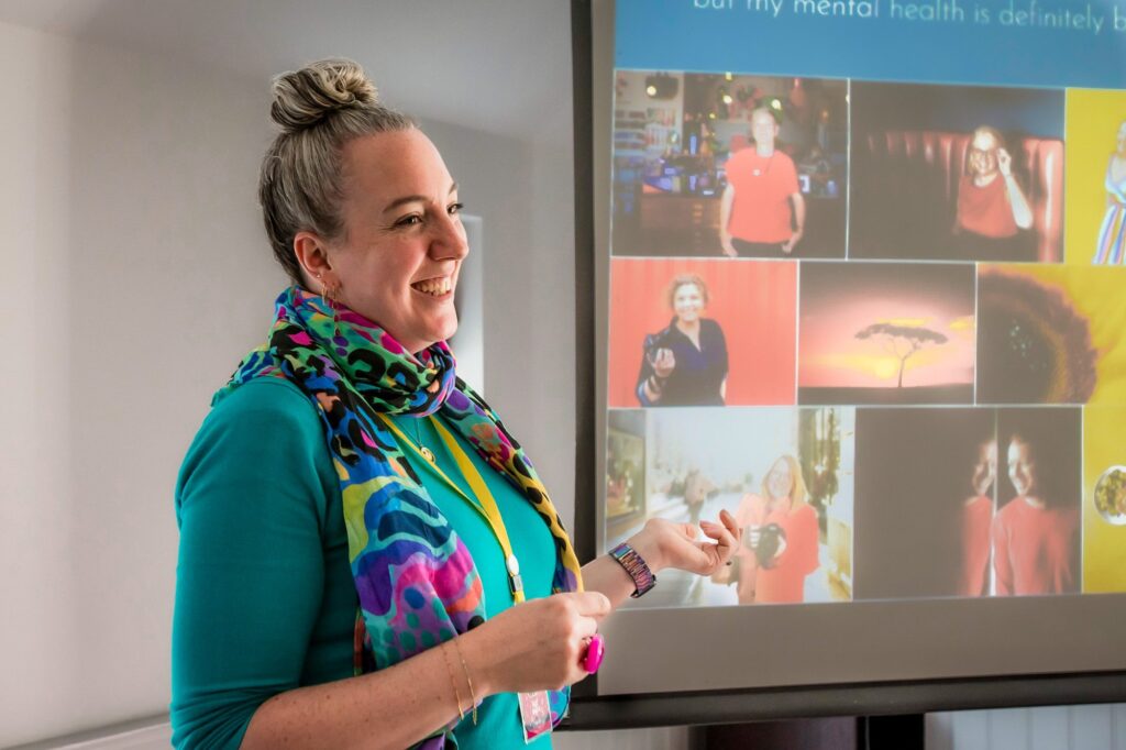 A white woman in a multi-coloured scarf and turquoise jumper is presenting at a photography conference.