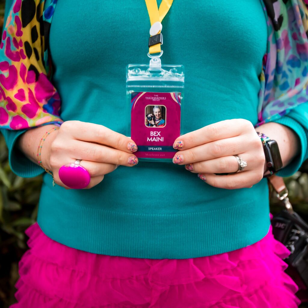 Close-up showing Bex Maini's TPV Guest Speaker conference pass against a turquoise jumper with colourful accessories.