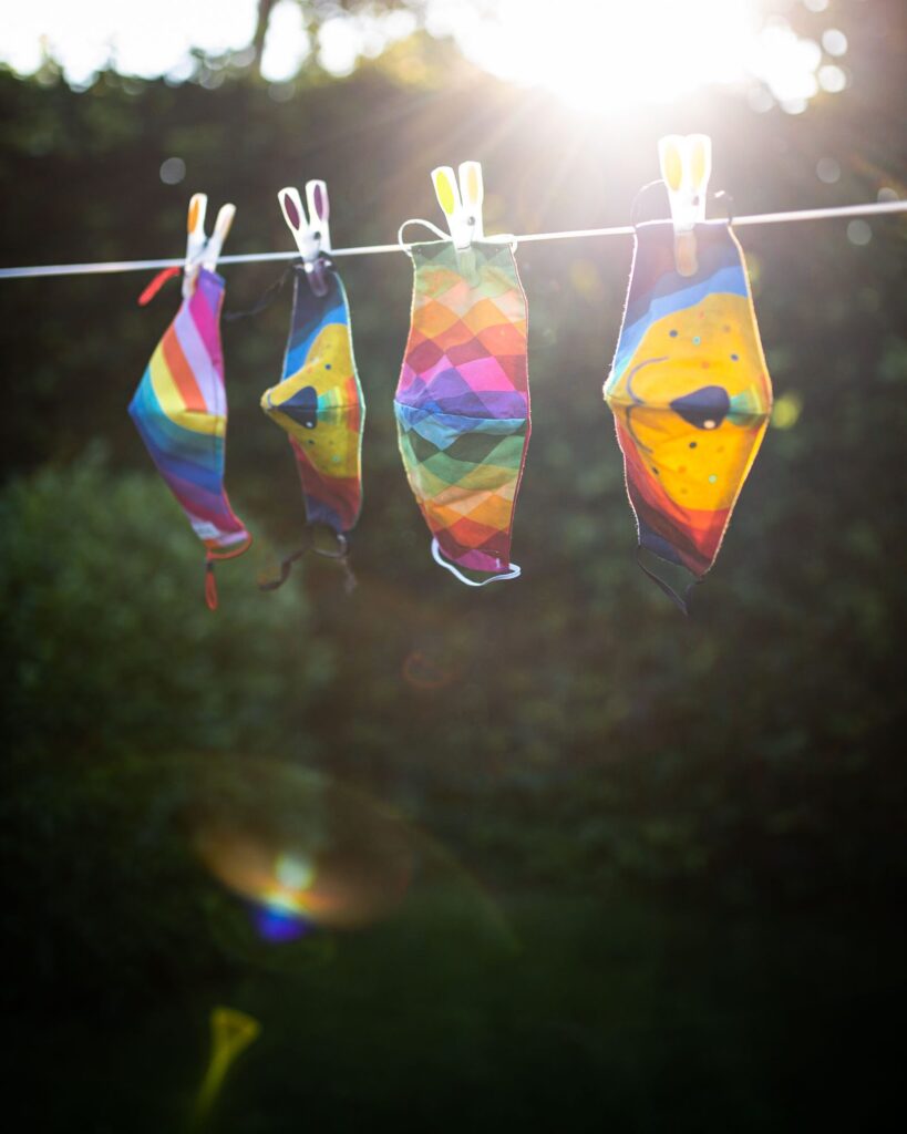 4 colourful masks hanging on the washing line with pegs in the sunshine with a sunflare beaming between them.