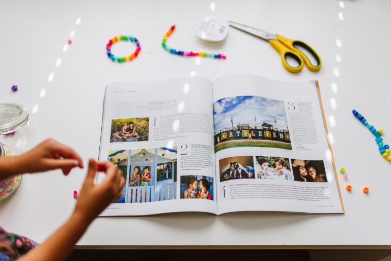 Click Magazine open to a spread featuring Bex's photos and words about photographing her twins. The magazine is on her white desk surrounded by rainbow beads and craft supplies with her daughter's hands making a bracelet.