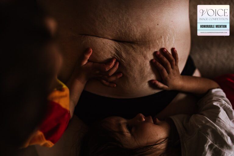 Twin children touching their Mum's stretch marks on her belly while they snuggle.