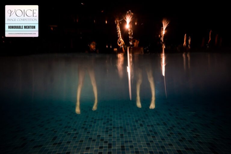 Underwater photograph in the dark, showing two sets of legs dangling in the pool water with lights reflecting from the above surroundings in Dubai.