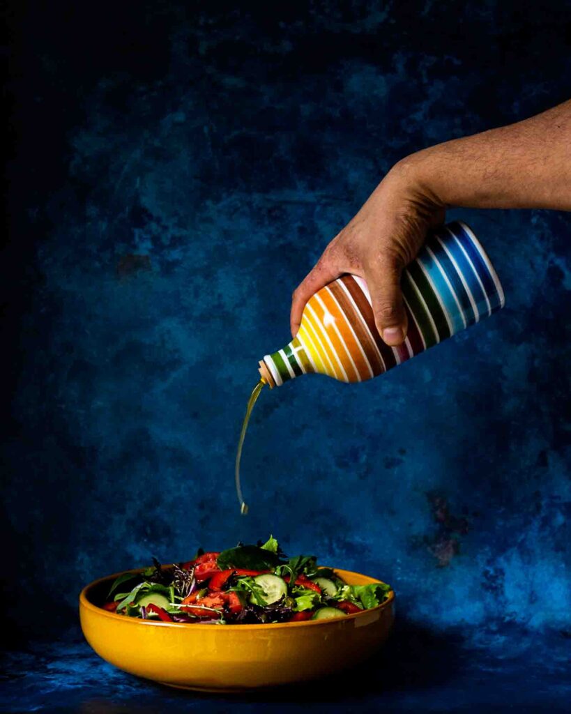 Salad in a yellow bowl with olive oil being drizzled on from a rainbow striped bottle