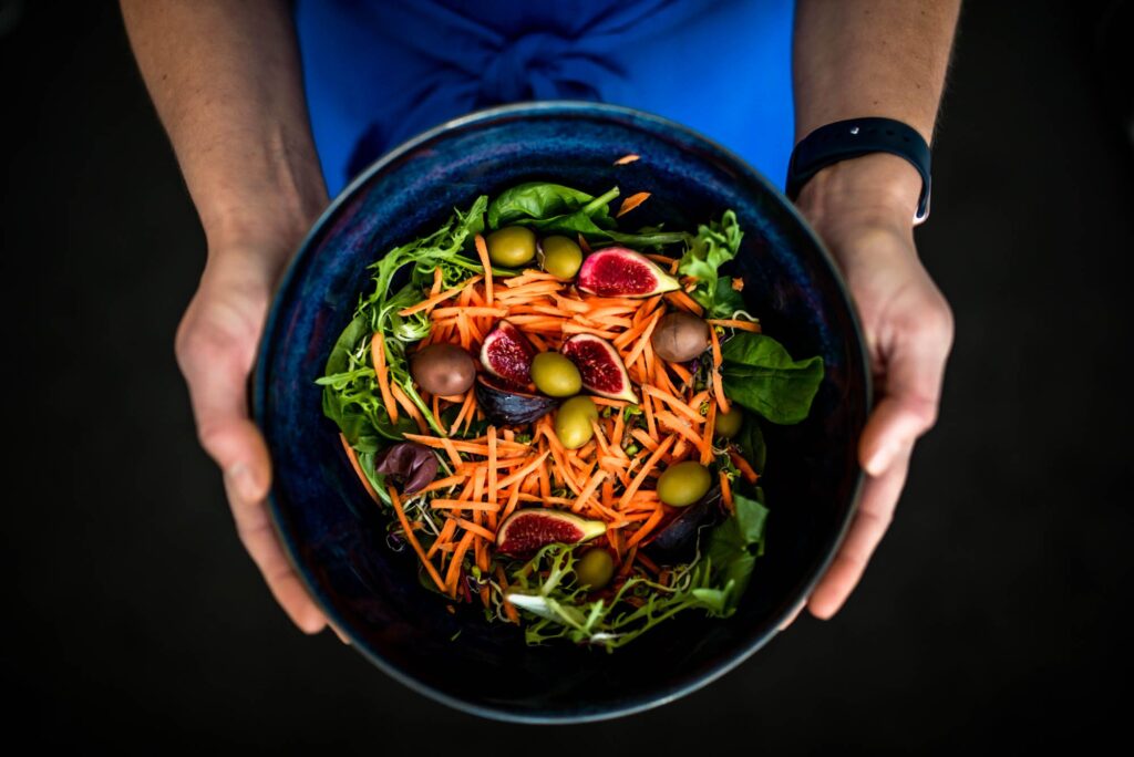 two hands holding a large bowl of colourful salad