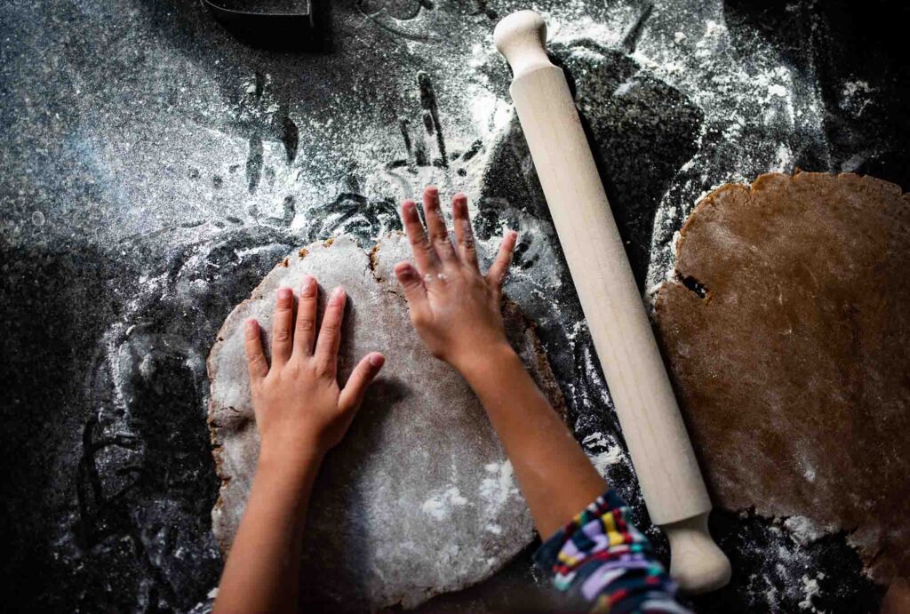Two hands of a child rolling out pastry with a rolling pin and lots of flour