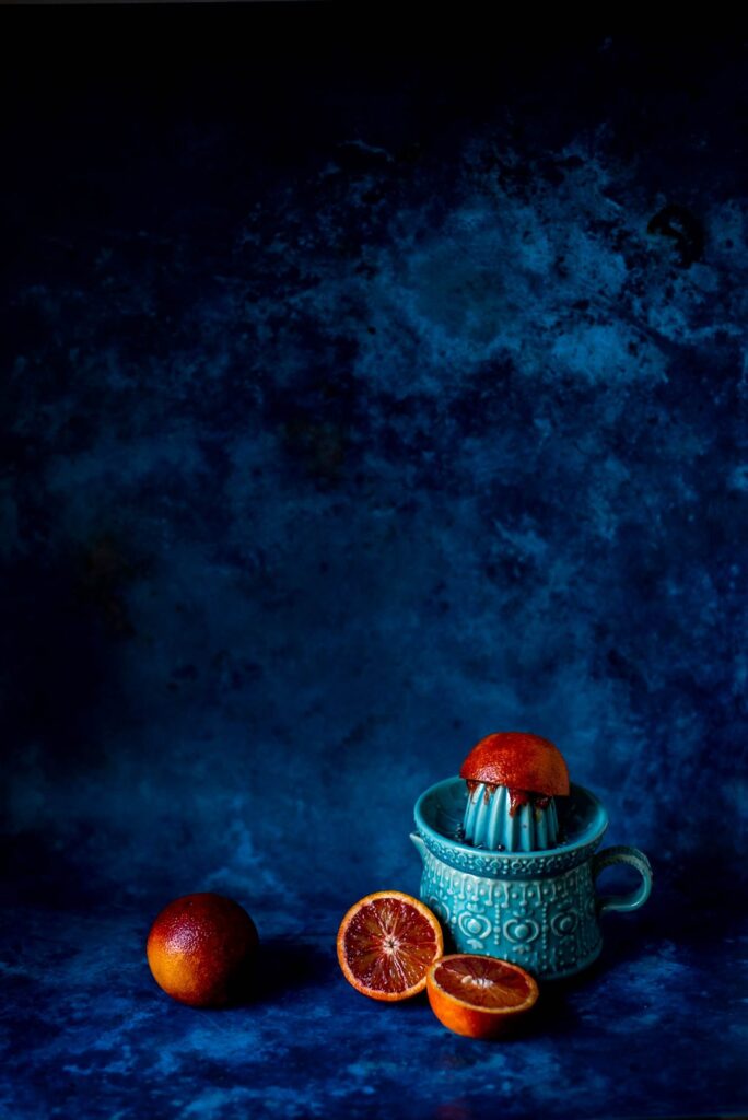 Blood Oranges on and around a turquoise juicer against a blue backdrop