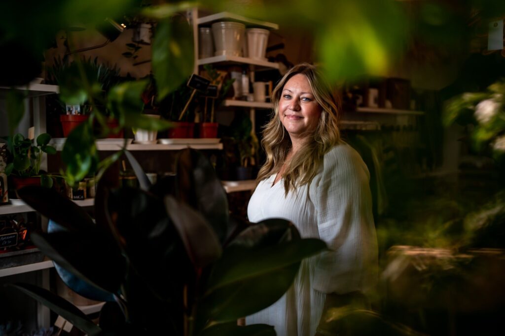 A white blonde woman with wavy hair, surrounded by plants in her gift shop in Lewes.
