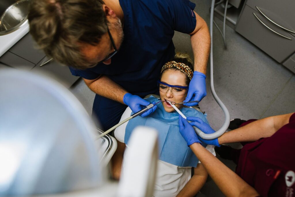 A female patient wearing a blue bib being worked on by a male dentist wearing blue gloves, with the dental light showing from above.