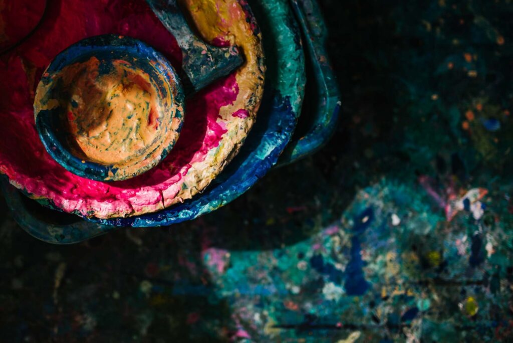 Abstract details of an artist's colourful floor covered in paint and palettes.