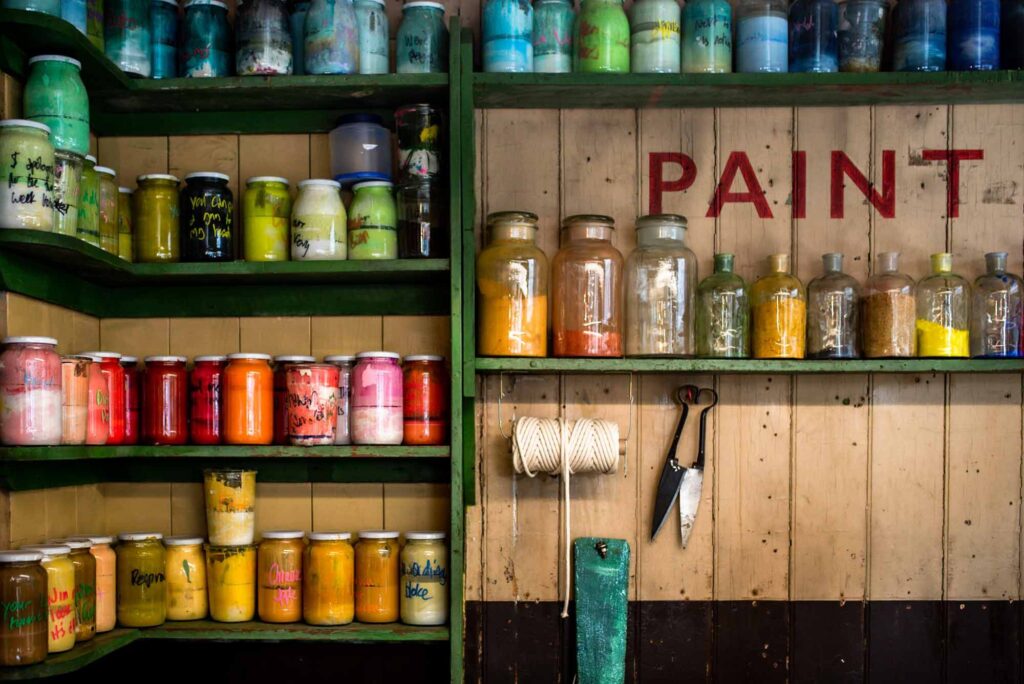 Rainbow coloured jars of paint pigment on wooden shelves in a paint shop
