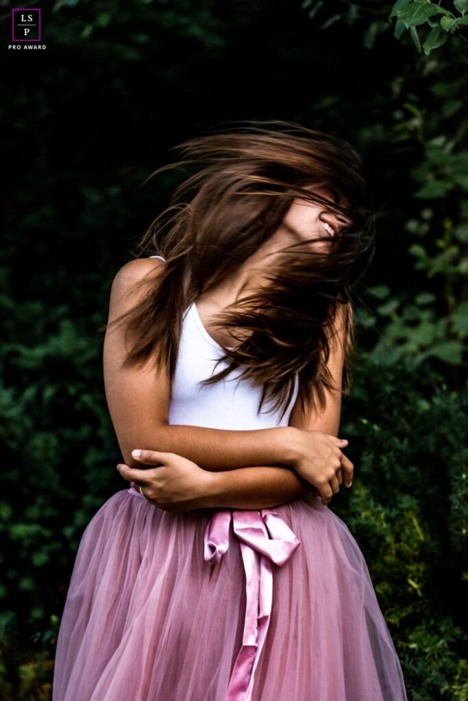 White brunette woman swishing her hair and wearing a pink tulle skirt and white vest top.