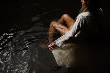 Model posing in a brown river wearing a white dress with her legs underwater