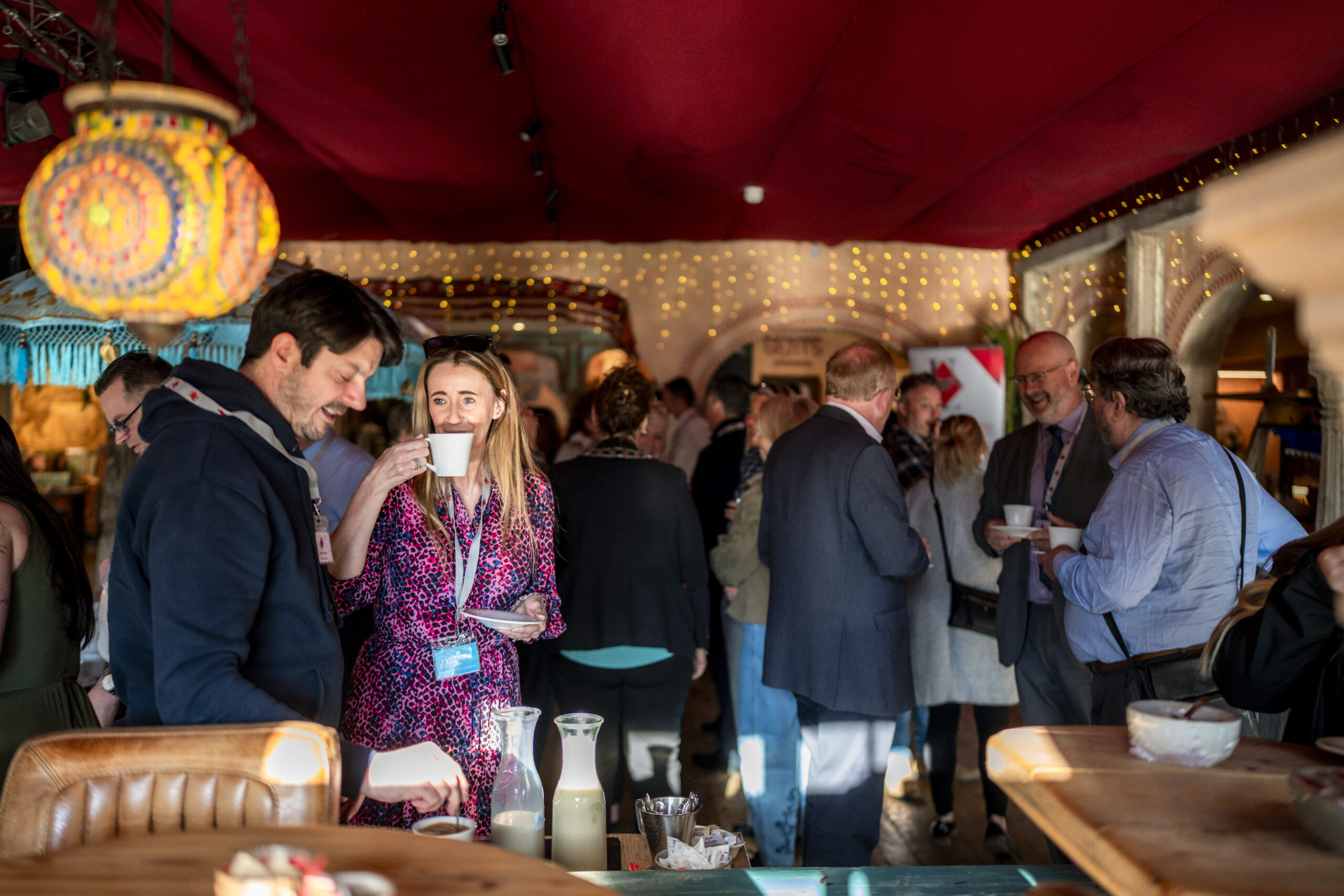 Business owners chatting with cups of tea and coffee in a lively room with a red ceiling, fairy lights and a colourful glowing lantern.