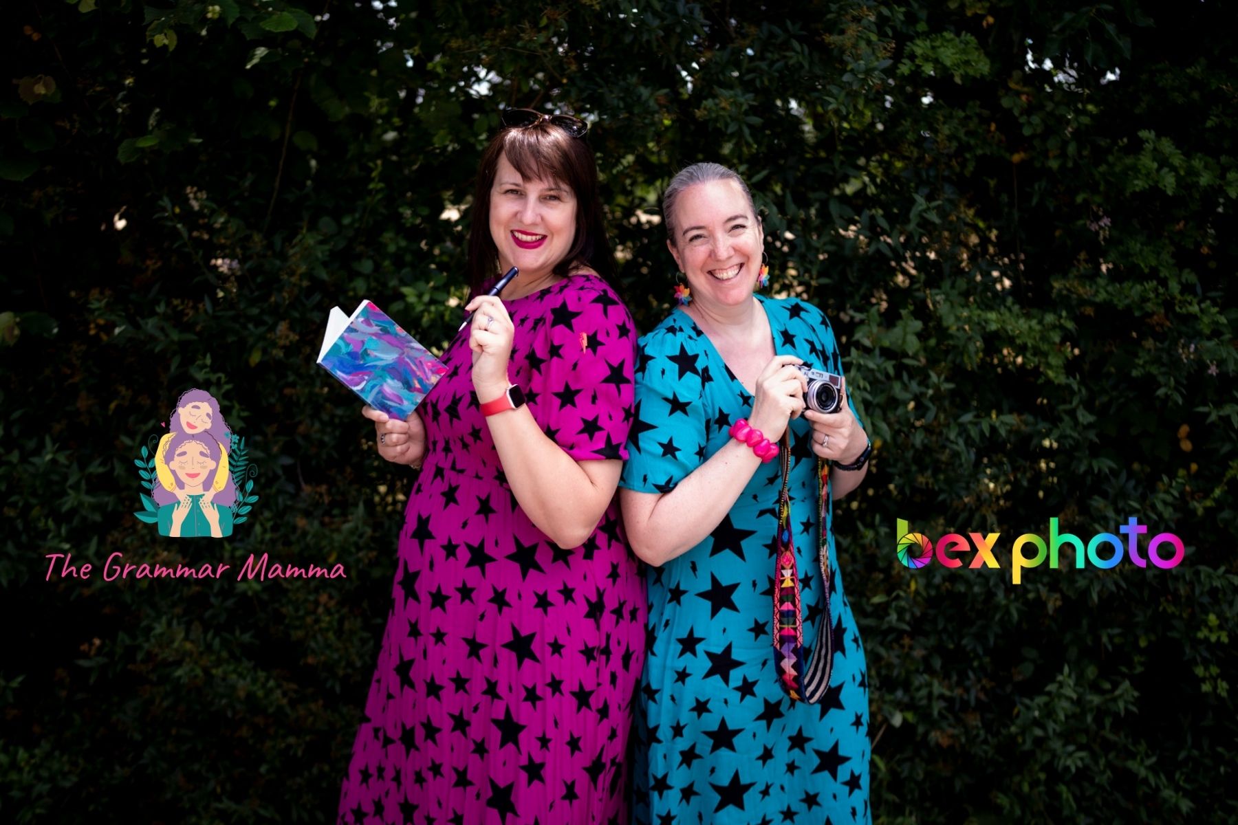 Two white women in Scamp & Dude star print colourful pink & teal dresses standing back to back, one holding a notebook and one has a camera. They each have their logos next to them, The Grammar Mamma and Bexphoto